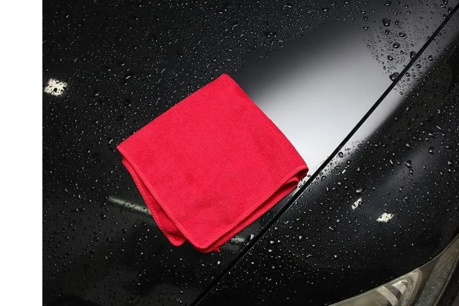 Water beading tightly on a protected paint surface beside a microfiber towel